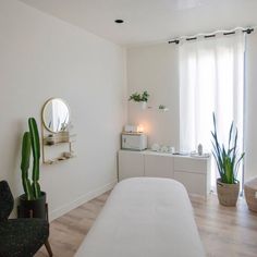 a white room with a bed, mirror and potted plant