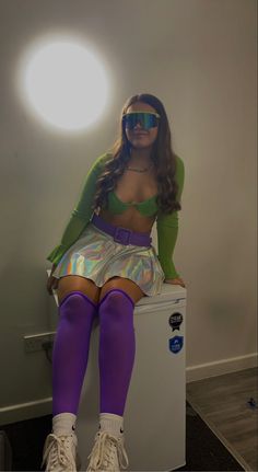 a woman in purple and green is sitting on top of a freezer with her legs crossed