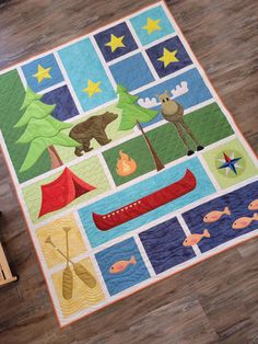 a child's quilt on the floor with animals and canoes in front of it