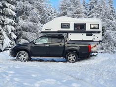 a truck with a camper on the back parked in front of snow covered trees