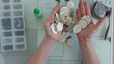 two hands are holding up several pieces of paper with buttons attached to them, while another person is working on some crafting supplies