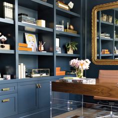 an office with blue bookcases and wooden desk in front of a gold framed mirror