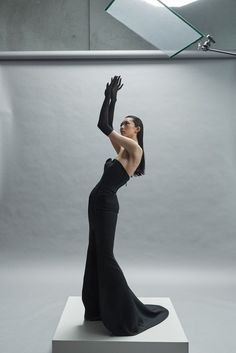 a woman in black dress standing on top of a white platform with her arms up