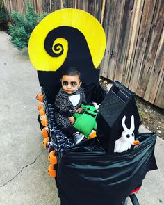 a little boy sitting in a costume on top of a cart filled with halloween items