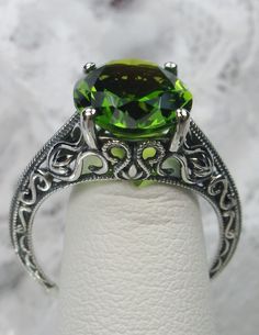 Natural Peridot Ring Swan Design#190 Custom Here we have an Art Deco inspired ring in 10k white gold, 14k white gold or solid sterling silver filigree with a Natural green peridot gemstone. This full cut oval cut 5ct peridot is 12mm in length and 10mm in width. The setting is 12mm NS on the finger. The inside of the band is marked 10k, 14k, or 925 for sterling (by choice). Notice the beautiful etched design of the silver filigree setting. A gift ring box is included and all rings are shipped in Classic Green Filigree Ring With Gemstone, Green Filigree Ring For Anniversary, Green Gemstone Filigree Ring For May Birthstone, Green Filigree Ring Hallmarked For Anniversary, Green Filigree Hallmarked Ring For Anniversary, Classic Green Filigree Ring As Gift, Green Filigree Ring As Fine Jewelry Gift, Green Filigree Ring Fine Jewelry For Gift, Green Emerald Ring With Intricate Design