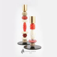 two tall vases with beads on top of each one and a gold cup in the middle