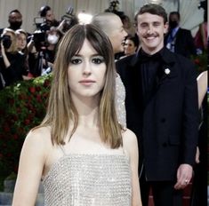 two people standing next to each other on a red carpet with cameras taking pictures behind them