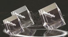 three clear glass trophies sitting on top of a black surface with white lines in the background