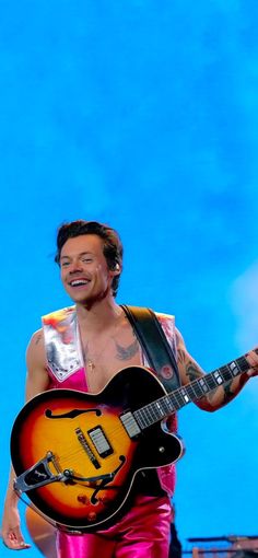 a man in pink pants holding a guitar and smiling at the camera while standing on stage