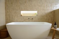 a white bath tub sitting in a bathroom next to a wooden stool and wall mounted mirror