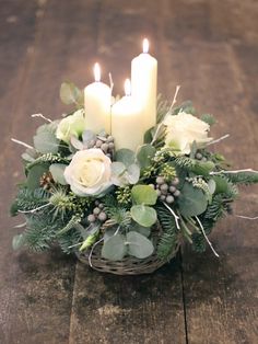 a basket filled with white flowers and candles on top of a wooden table covered in greenery