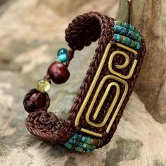 A spiral pendant made of brass centers this wristband bracelet with crocheted brown cord that circles the wrist. Tiraphan Hasub of Thailand crafts the bracelet accenting the pendant with petite beads of reconstituted turquoise. The bracelet closes with an adjustable button clasp made of rain tree wood adorned with colorful glass beads.