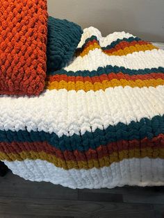 a crocheted blanket on top of a bed next to an orange and white pillow