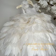 a dress made out of white feathers sitting on top of a wooden shelf next to flowers