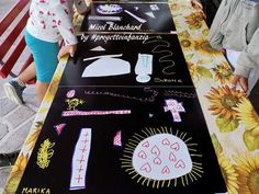 two children standing at a long table with drawings on it and sunflowers in the background