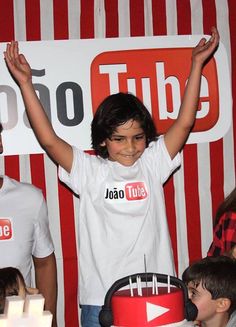 a young boy standing in front of a red and white cake