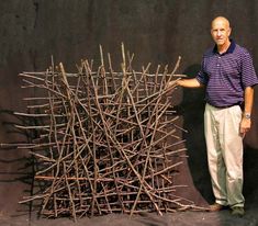 a man is standing next to a sculpture made out of sticks and wood strips that are stacked on top of each other