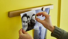 a person is holding an open photo frame on a yellow wall with two photos hanging from it