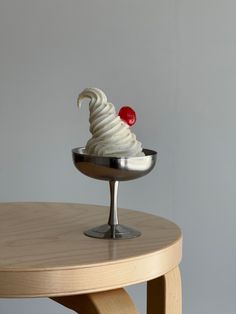 an ice cream sundae with a cherry on top sits in a bowl atop a wooden table