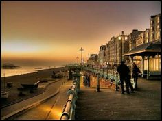 people are walking along the boardwalk at sunset