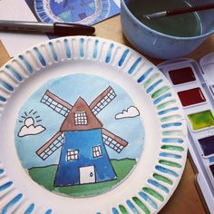 a paper plate with a windmill painted on it next to paintbrushes and watercolors