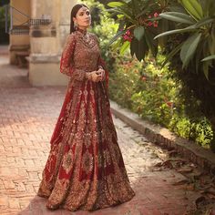 a woman in a red and gold bridal gown standing on a brick walkway next to flowers