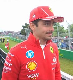 a man in a red jacket and hat standing next to a fence at a race track