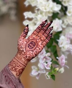 a close up of a person's hand with henna on it and flowers in the background