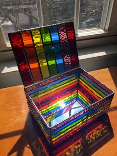 a multicolored box sitting on top of a wooden table next to a window