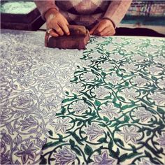 a woman is working on an intricately designed piece of fabric with a wood block