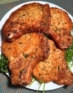 four pieces of fried meat on a white plate with parsley sprigs and garnishes