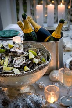 an outdoor table set with champagne and oysters in a bowl, candles and plates