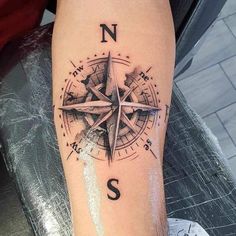 a compass tattoo with the letter s on it's leg and an arrow in the middle