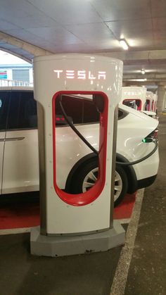 an electric car charging station with two cars in the background and one is plugged up