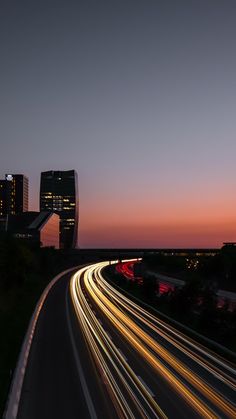 the city skyline is lit up at night with long exposure and light streaks on the road