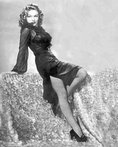 a woman in a short dress leaning on a rock