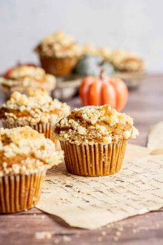 several muffins are sitting on top of a piece of parchment paper next to some pumpkins