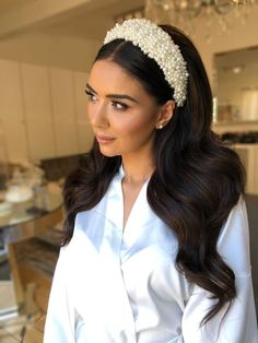 a woman with long hair wearing a white shirt and pearl headband, standing in front of a chandelier