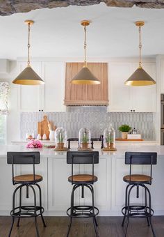 three stools sit at the center of a kitchen island with two pendant lights hanging over it