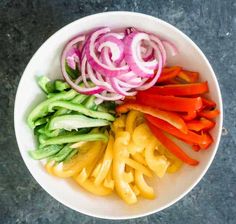 a white bowl filled with sliced vegetables on top of a gray counter next to a knife