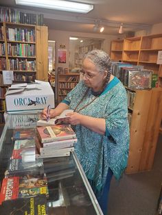 a woman standing in front of a book shelf filled with books and holding a pen