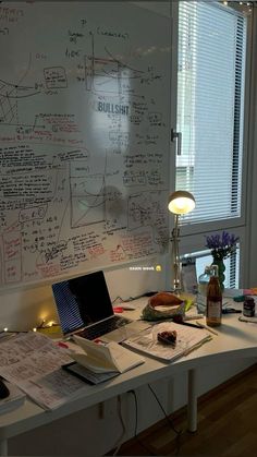 a white board with writing on it next to a lamp and desk in front of a window