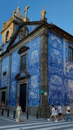 people walking on the sidewalk in front of a building painted with blue and white tiles