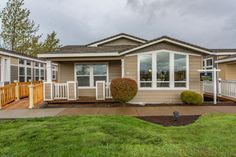 a mobile home sits in the front yard on a cloudy day with green grass and shrubs