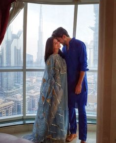 a man and woman standing next to each other in front of a window looking at the city