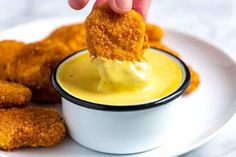 a person dipping something into a small white bowl filled with yellow sauce on top of chicken nuggets