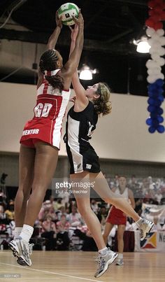 two women playing basketball in an indoor arena with people watching from the stands and onlookers