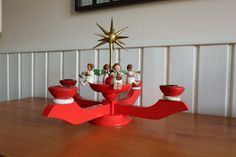 a wooden table topped with red bowls and figurines next to a christmas tree