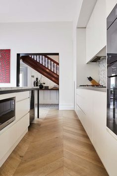 an open kitchen with white cabinets and wood flooring, along with stairs leading up to the second floor