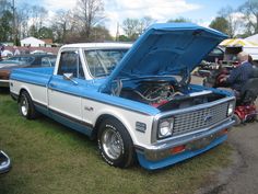 an old blue and white pickup truck with its hood open on display at a car show